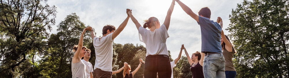 © iStock.com/lorenzoantonucci Gruppe von Freunden im Park, die sich an den Händen halten und in den Himmel steigen.