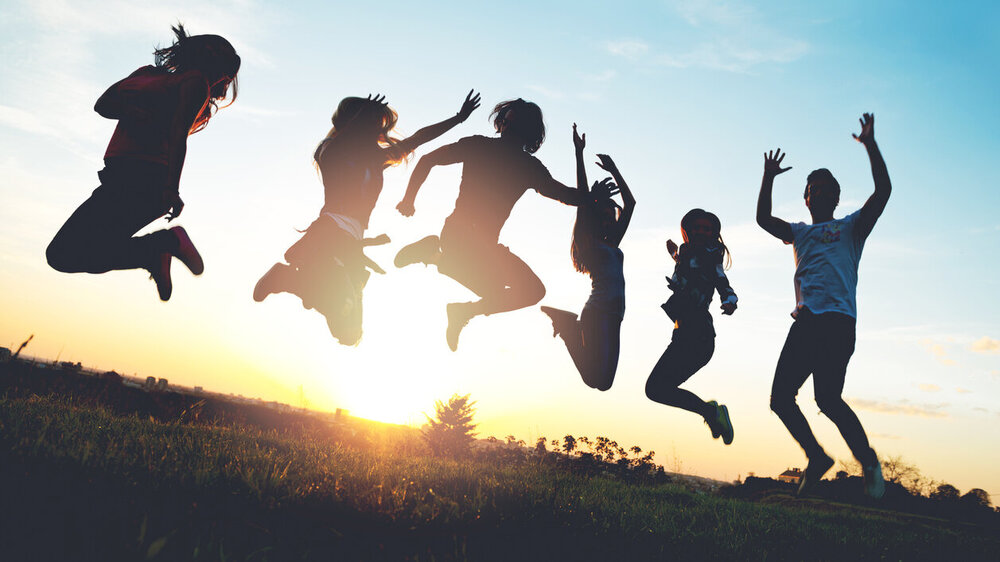 © iStock.com/Tijana87 Gruppe von Menschen, die im Freien springen; Sonnenuntergang