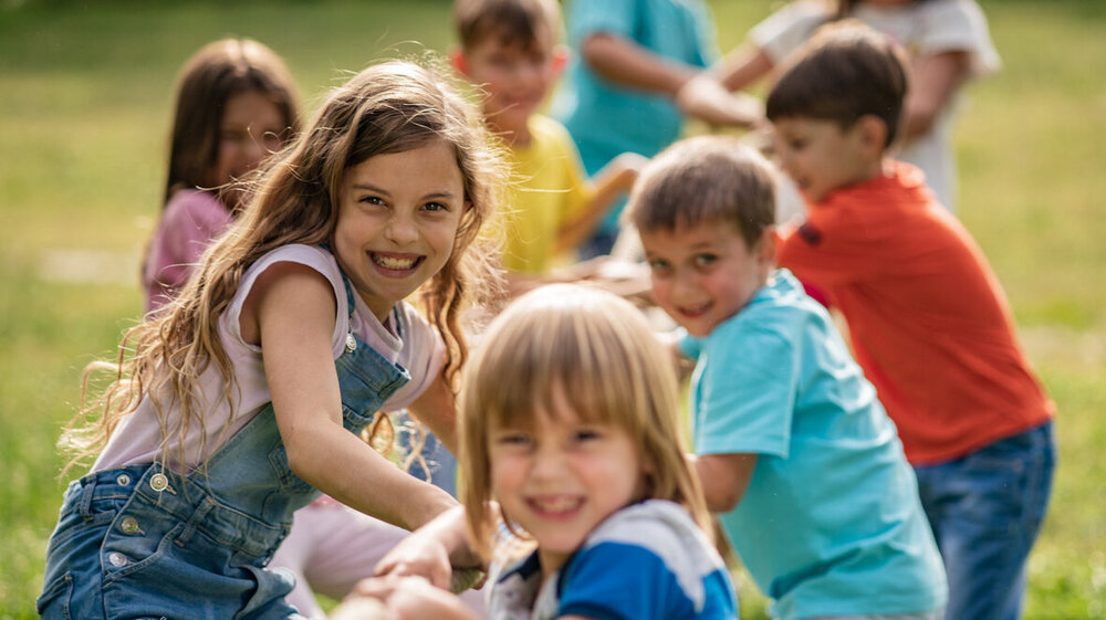 © iStock.com/StockPlanets Lächelnde Kinder, die ein Seil im Park ziehen